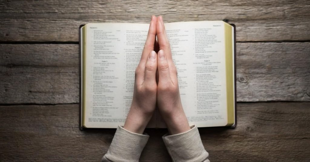 Hands praying over an open Bible for strength